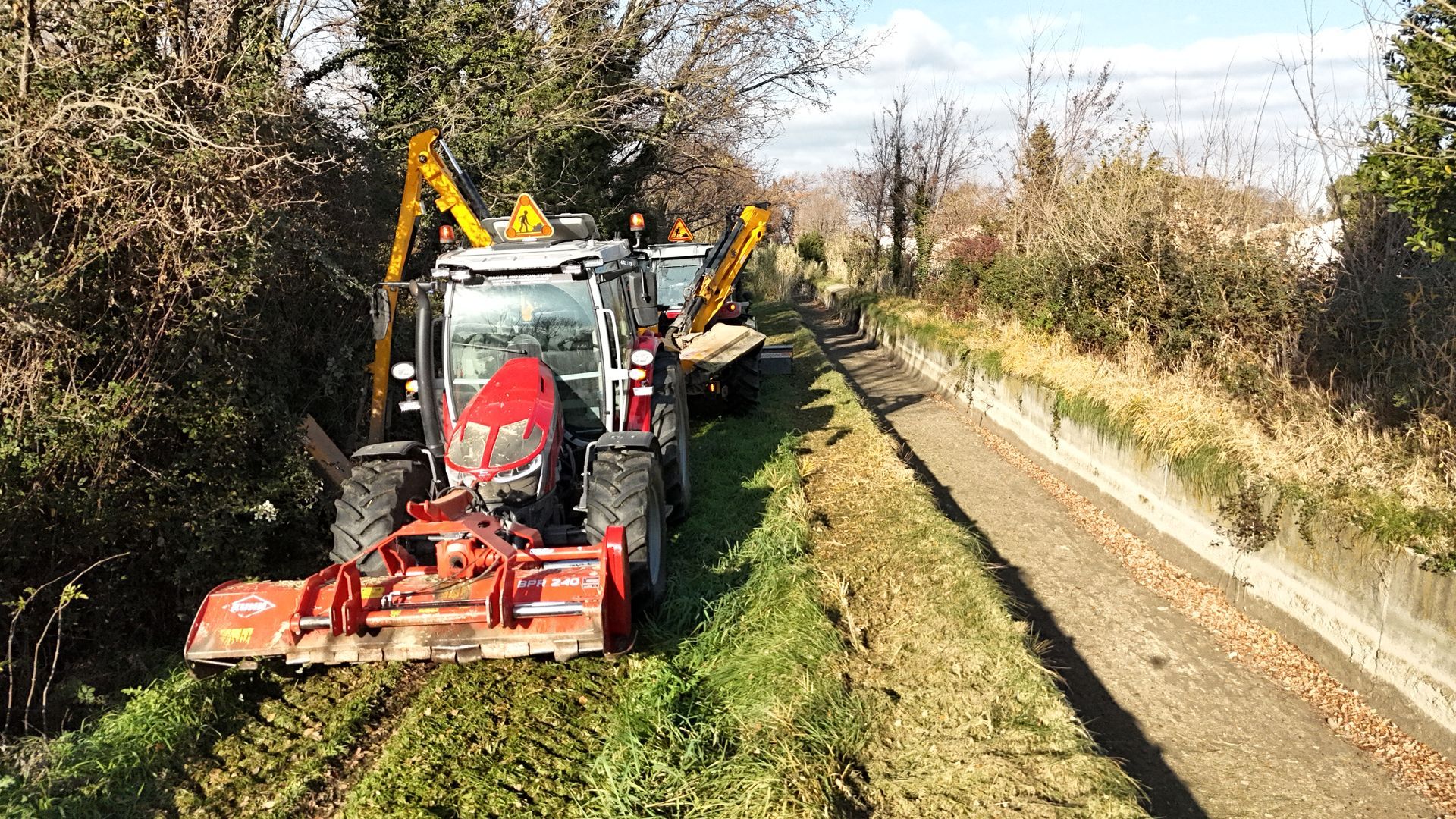 Tracteurs avec broyeurs et bras faucheurs en action pour le débroussaillage et l’entretien des abords d’un canal.
