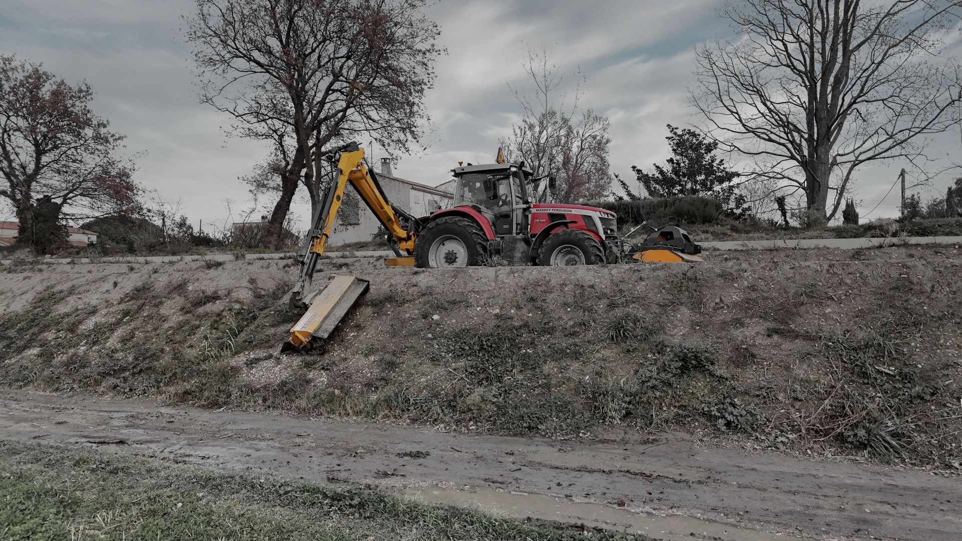 Tracteur rouge équipé d’un bras de débroussaillage hydraulique intervenant sur une berge pour l’entretien des espaces naturels et fossés.