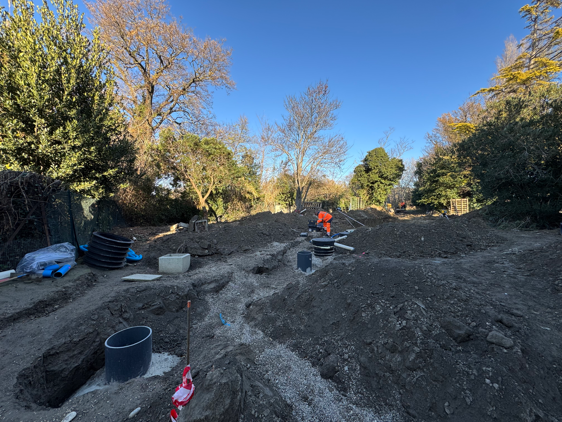 Chantier d’assainissement avec tranchées, canalisations et regards en cours d’installation dans un grand terrain arboré.