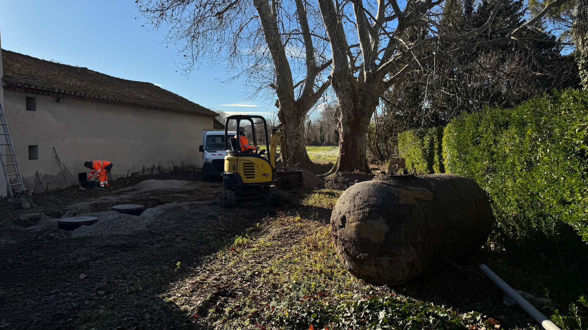 Travaux de terrassement pour la pose de regards d’assainissement, avec une mini-pelle et des techniciens sur un chantier extérieur.