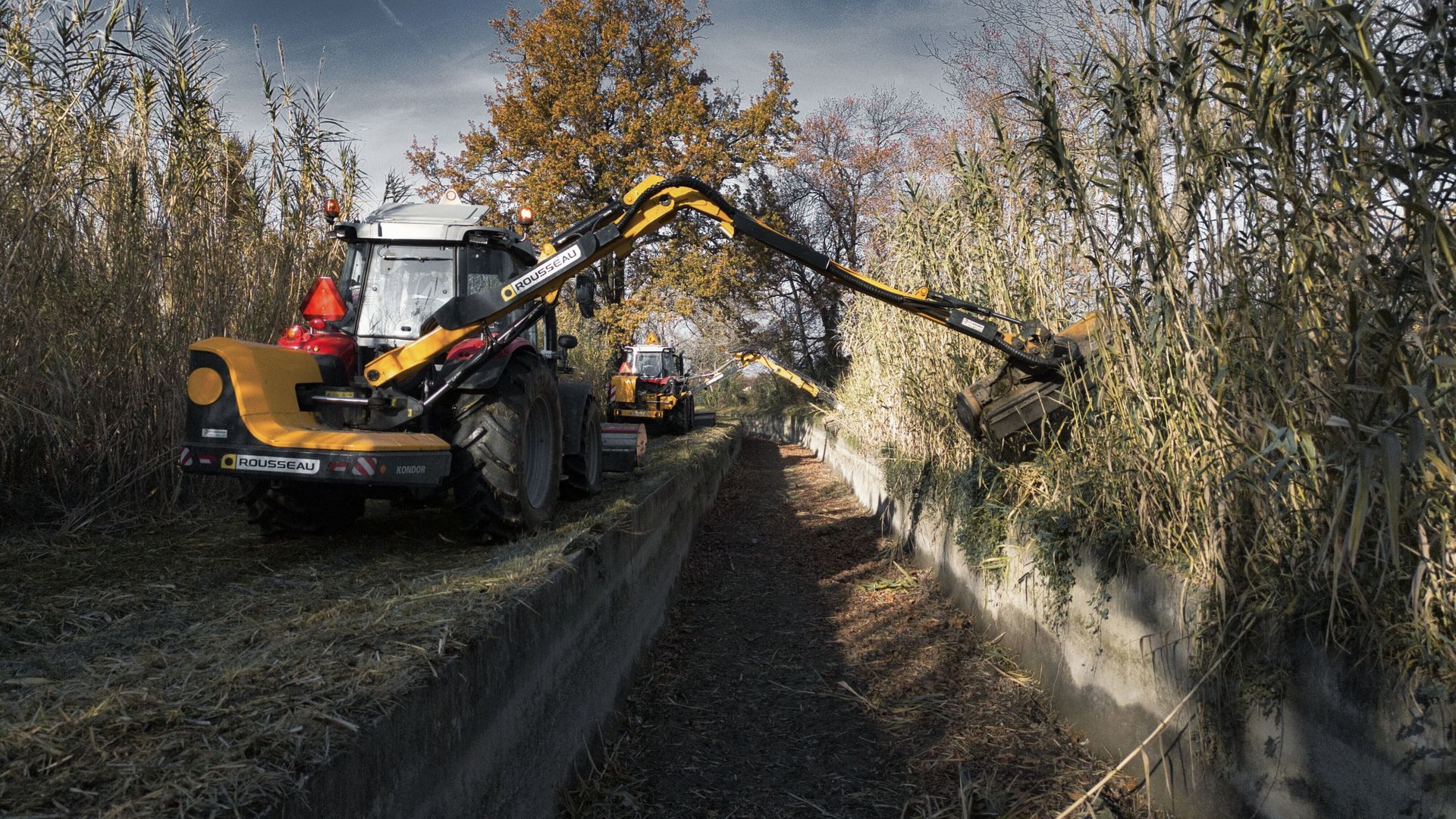 Tracteur équipé d’un bras de débroussaillage hydraulique en action pour nettoyer un fossé bordé de végétation dense. Intervention professionnelle d’entretien des canaux.