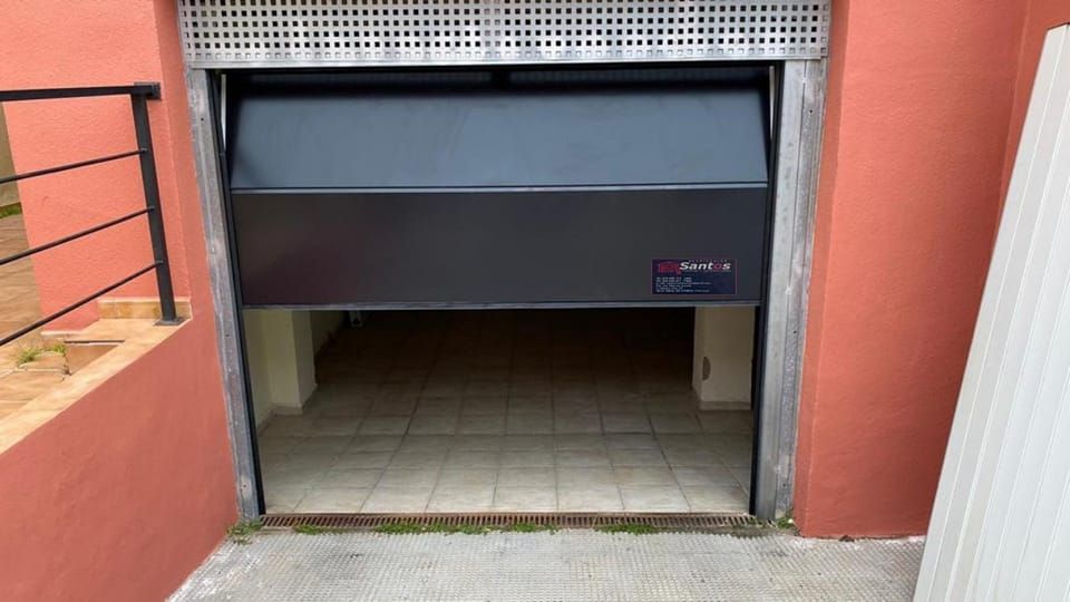 Una puerta de garaje negra está abierta a un garaje vacío.