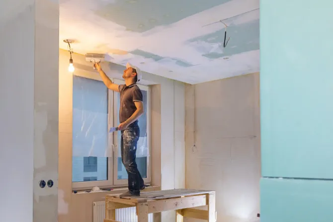 Un hombre está pintando el techo de una habitación con un rodillo.