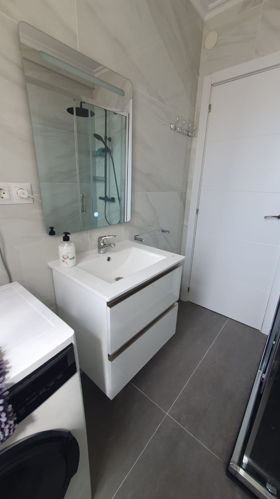 Un baño con lavabo, espejo, lavadora y secadora.