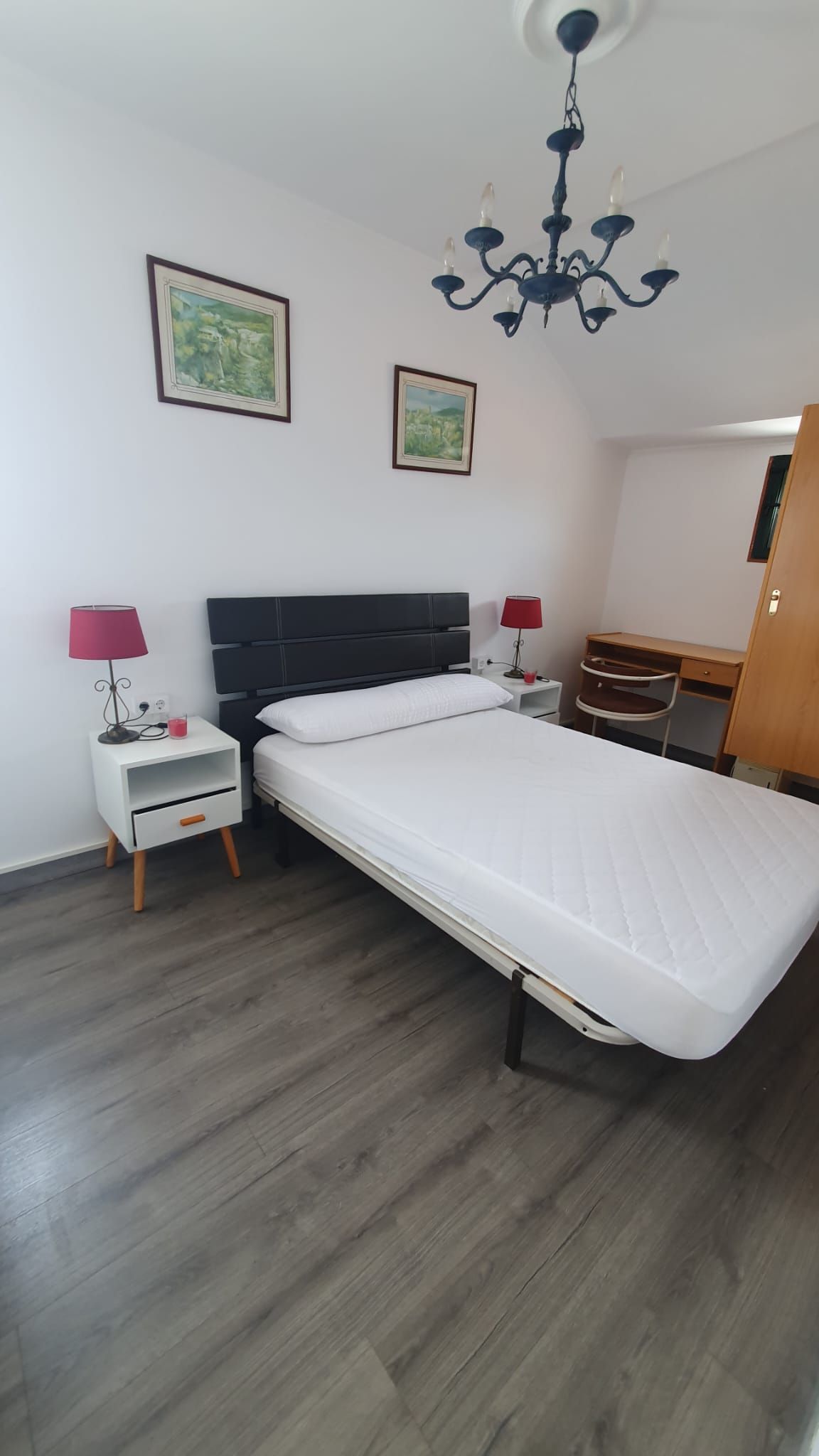 Un dormitorio con una cama, mesita de noche, lámparas y una lámpara de araña.