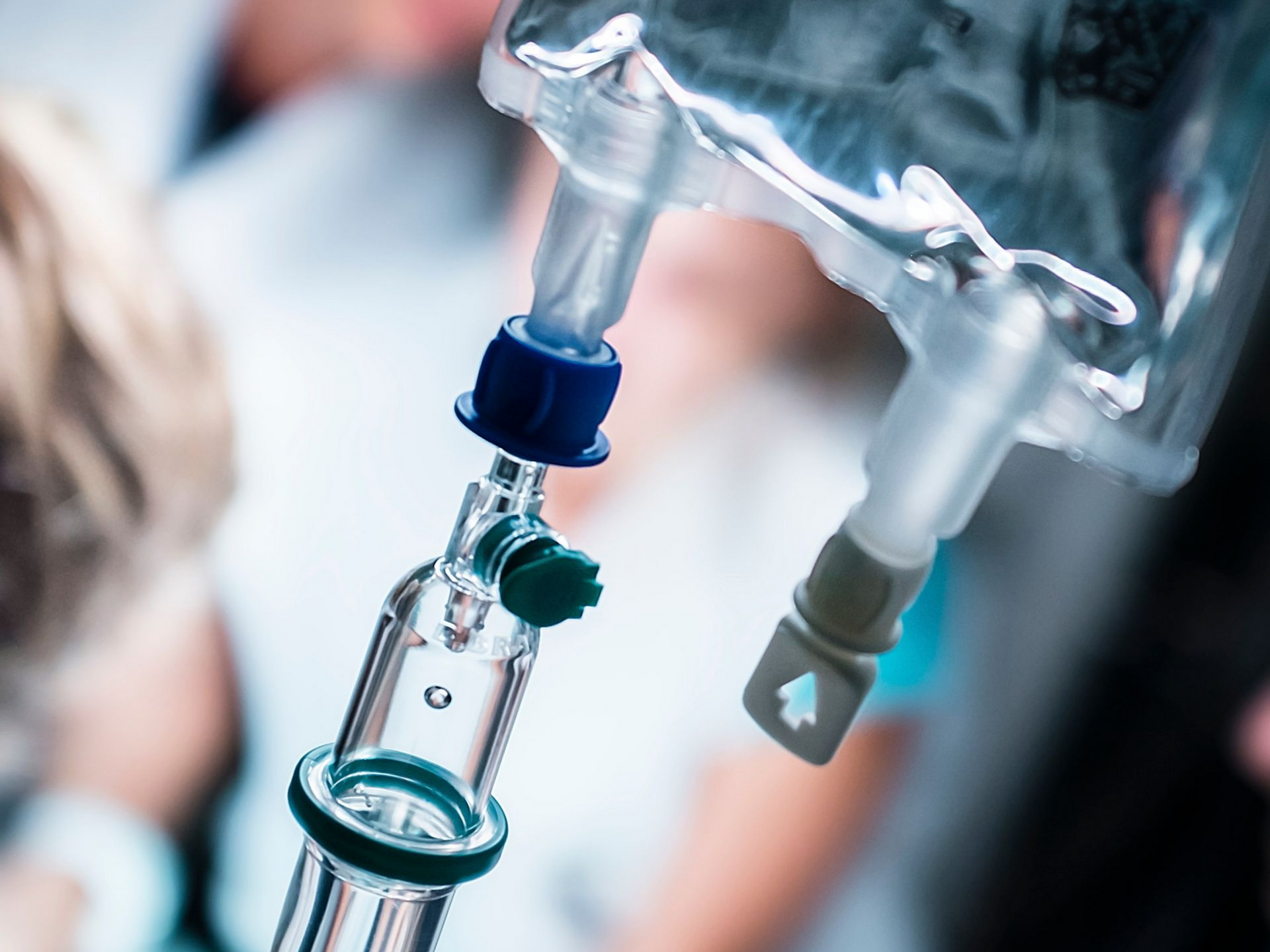 Poche de perfusion suspendue, tubulure connectée. Patient flou à l'arrière-plan.