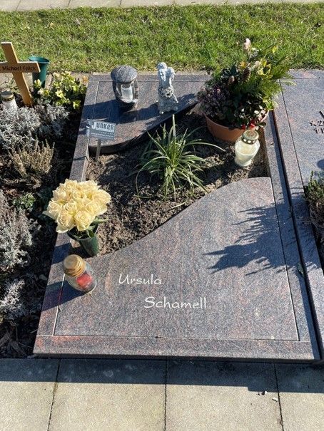 Ein Grab mit Blumen, Kerzen und einem Kreuz darauf.