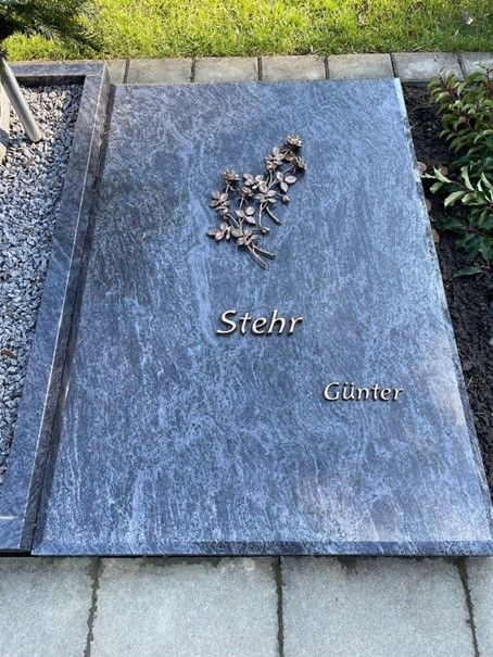 Auf einem Bürgersteig steht ein Grabstein mit Blumen darauf.