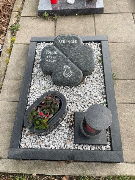Ein Grabstein für Springer ist von Kies und Blumen umgeben