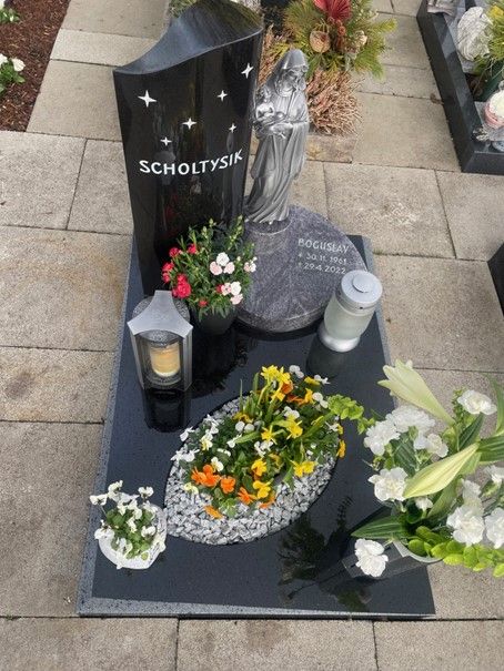 Ein Grab mit Blumen und Kerzen und dem Namen Scholtynk darauf