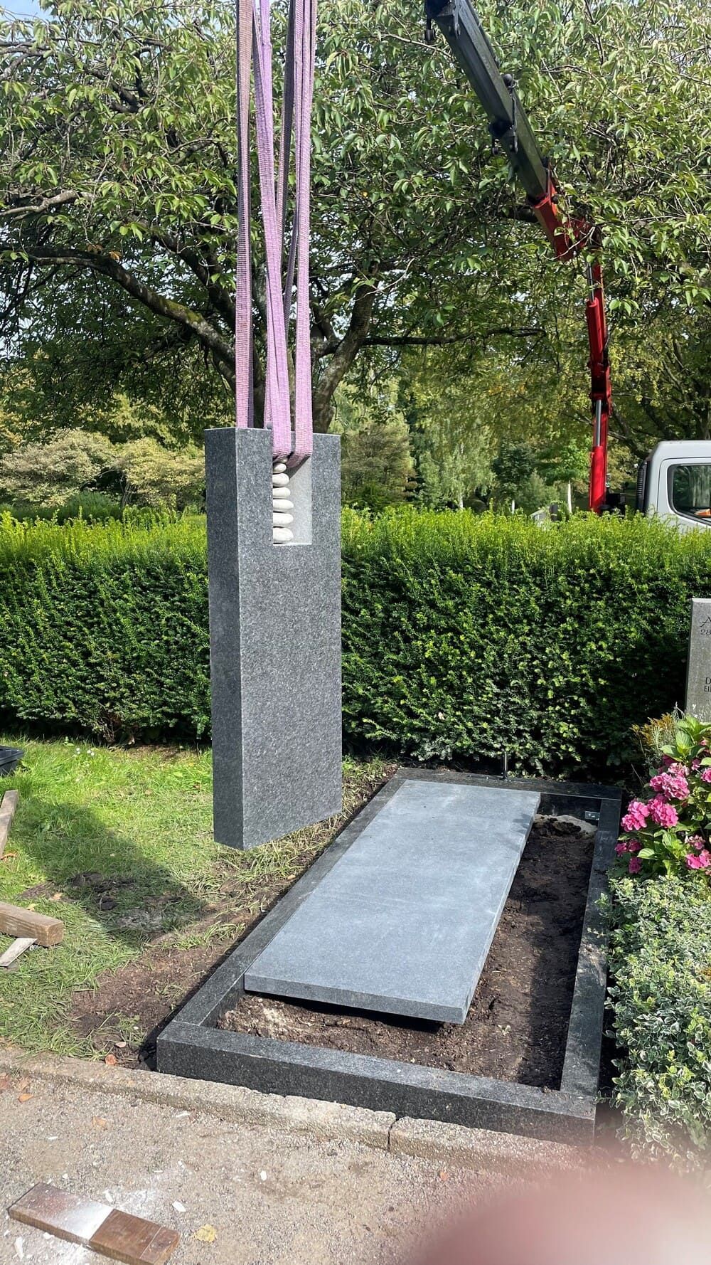 Ein Kran hebt einen Grabstein auf einem Friedhof  | ZIESCHE // GRABMALE