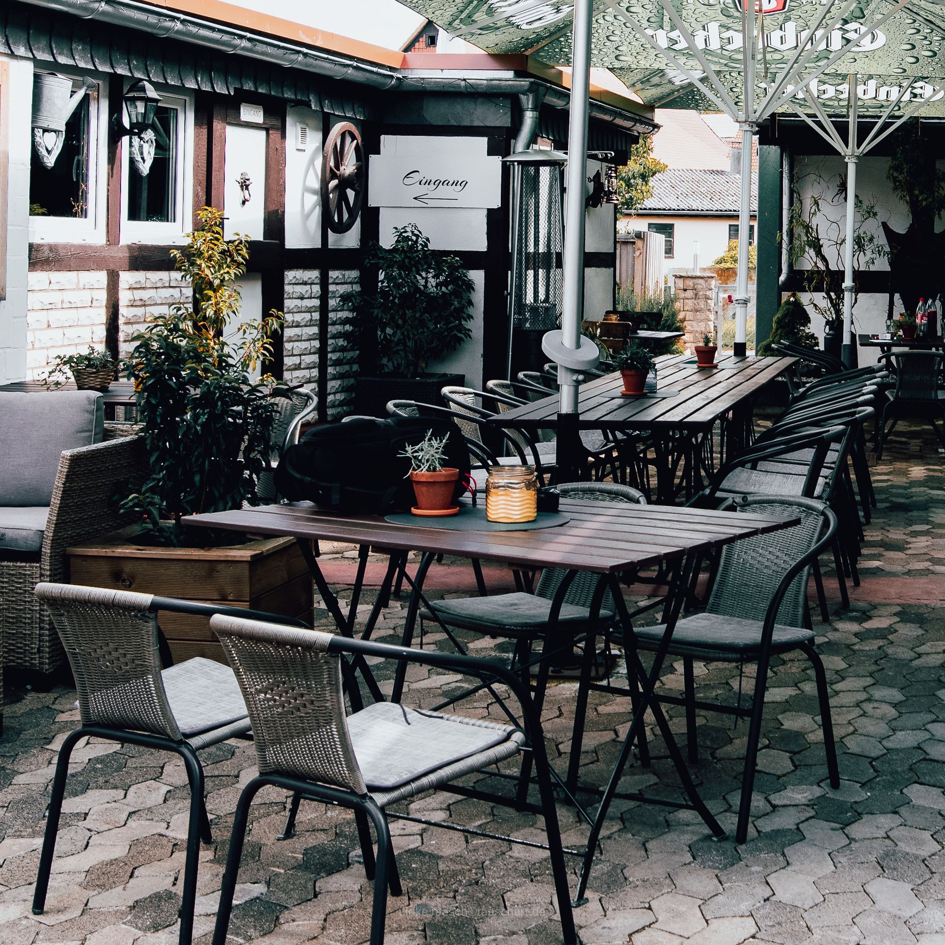 Außenbereich eines Restaurants mit Tischen, Stühlen und Topfpflanzen vor der Kulisse eines Fachwerkgebäudes.