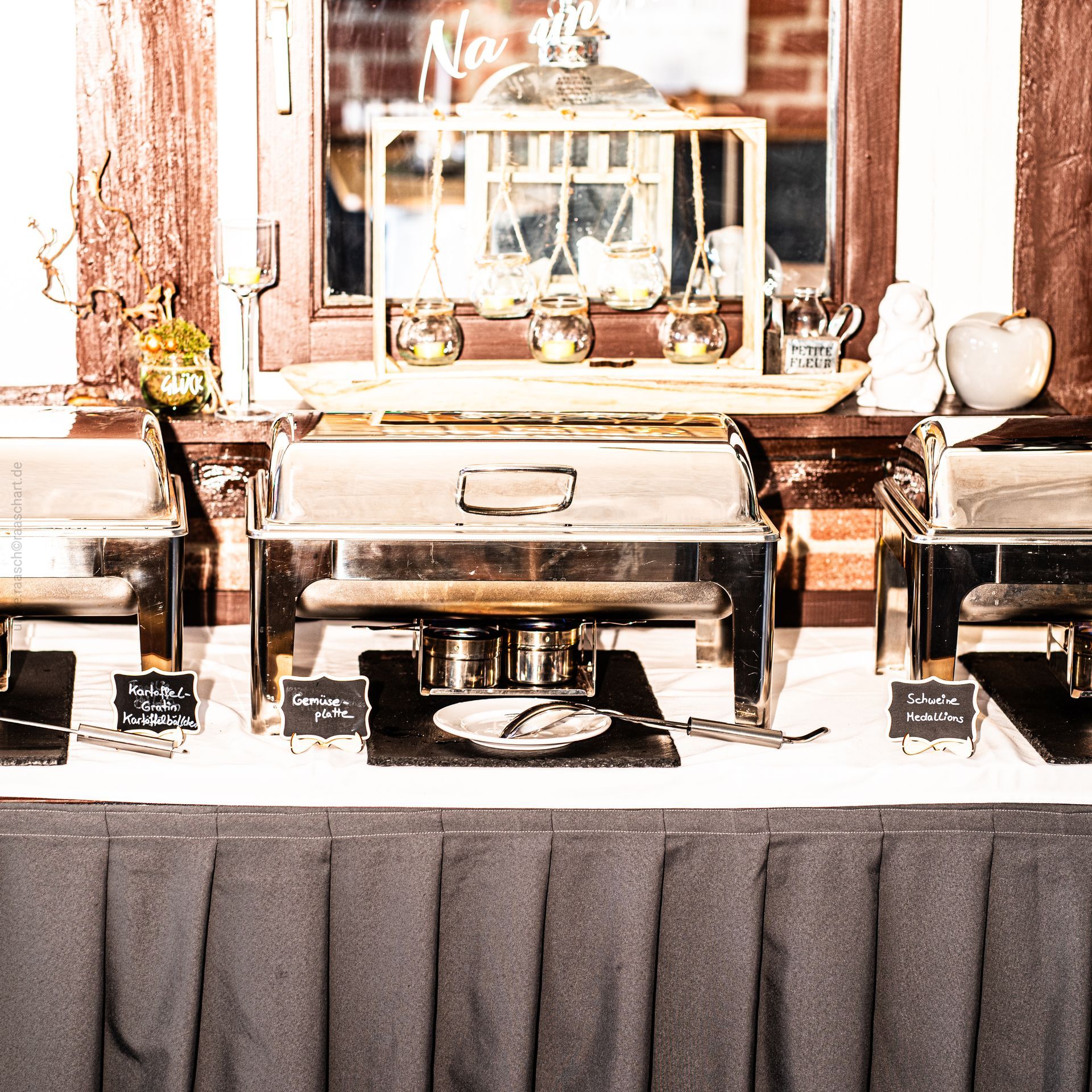 Buffet-Tisch mit Speisenwärmern aus Edelstahl, bedeckt mit grauem Stoff.