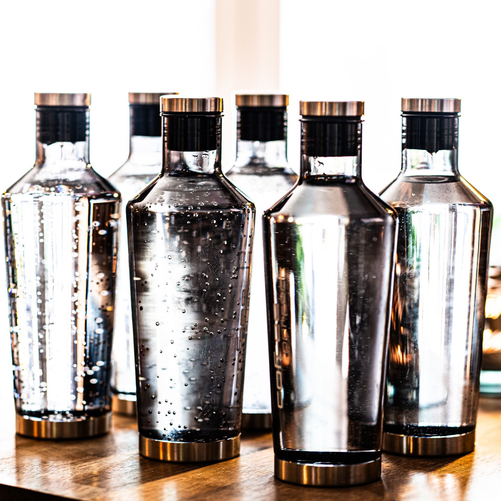 Sechs durchsichtige Glasflaschen mit silberner Metallbeschichtung und Messingakzenten auf einem Tisch.