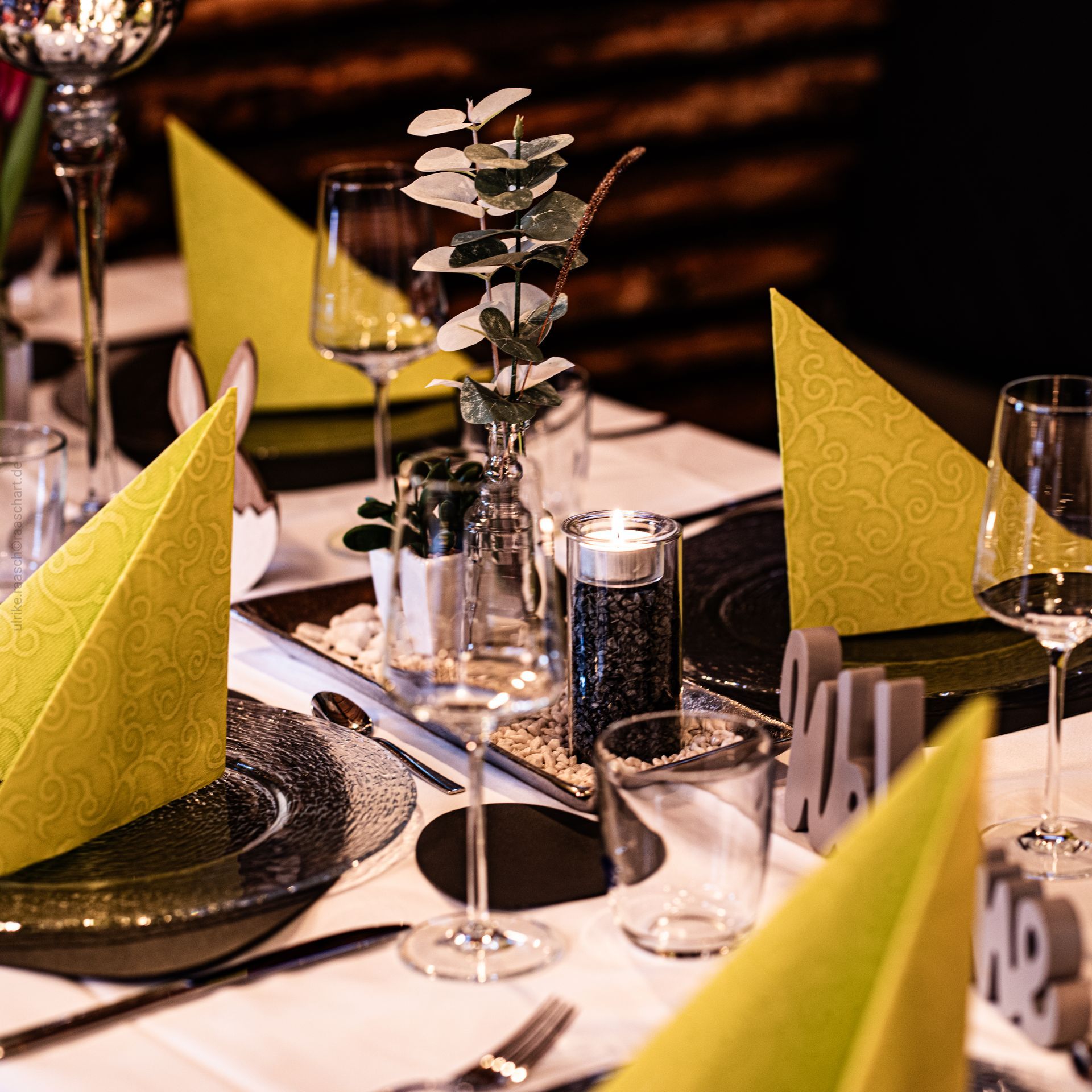 Tischdekoration mit gelben Servietten, Gläsern und Dekorationselementen.