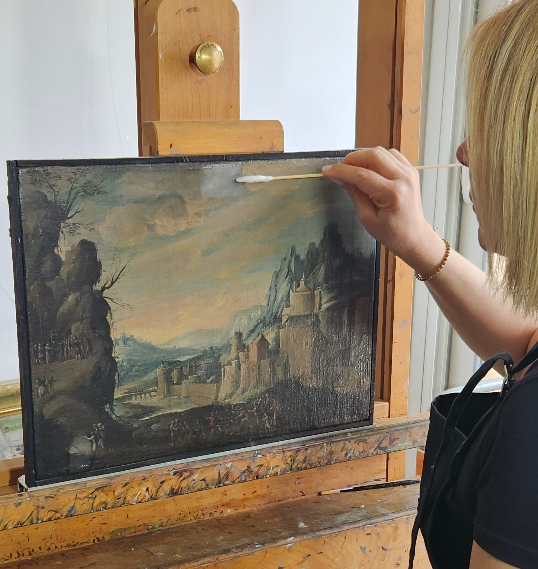 Restauratrice en train de rénover un tableau représentant un château fort.