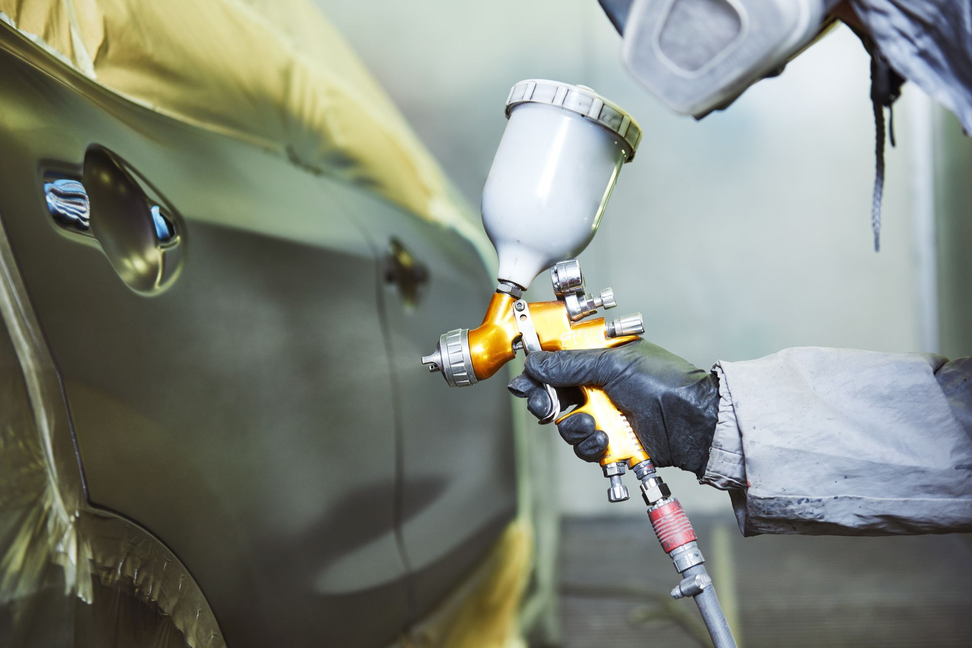 Un peintre utilise un pistolet à peinture pour appliquer de la peinture jaune sur une voiture dans un atelier.