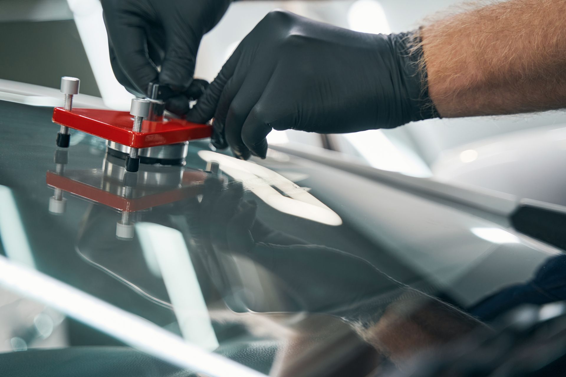 Des mains gantées inspectent un pare-brise de voiture avec un outil de réparation rouge fixé.