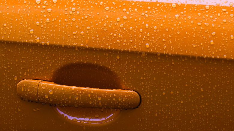 Poignée de portière orange recouverte de gouttes de pluie, avec un léger reflet violet en dessous.