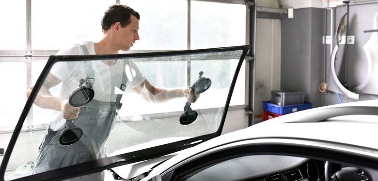Un homme nettoie le pare-brise de sa voiture à l'intérieur avec des outils à ventouses pour vitres.