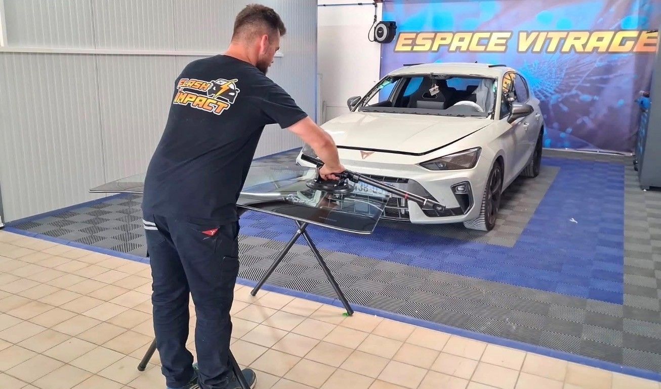 Un ouvrier en combinaison de protection peint une portière de voiture au pistolet dans une cabine de peinture.