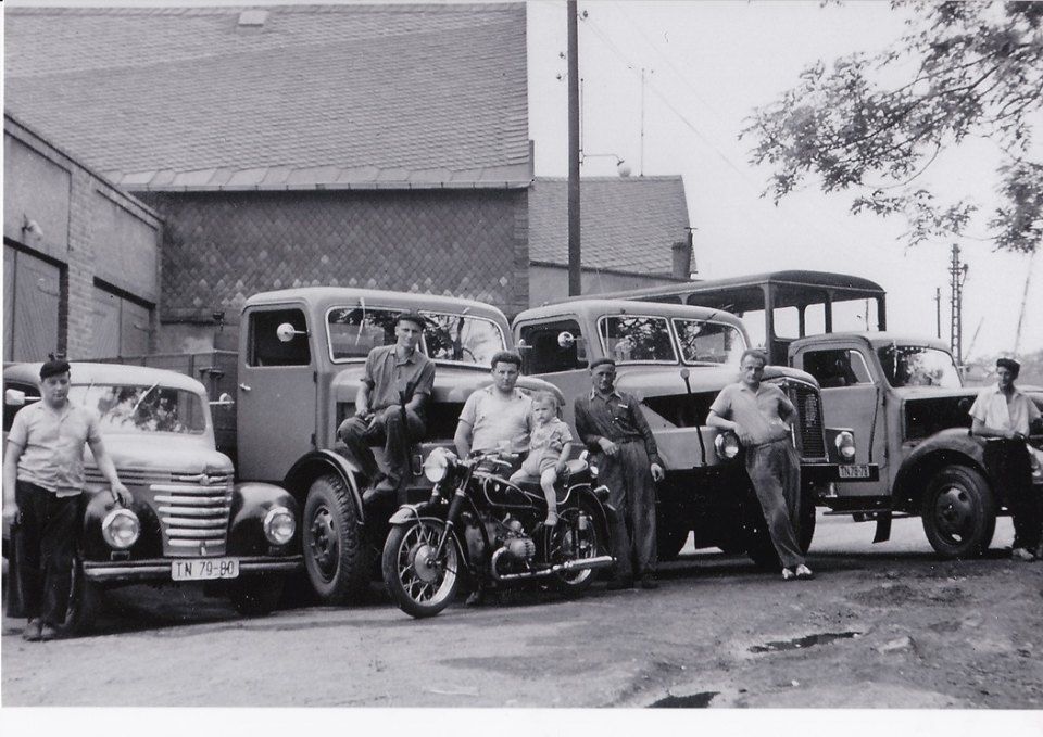 Altes Schwarz-Weiß-Foto von Oldtimern und Motorrädern, die neben einem Backsteingebäude geparkt sind.
