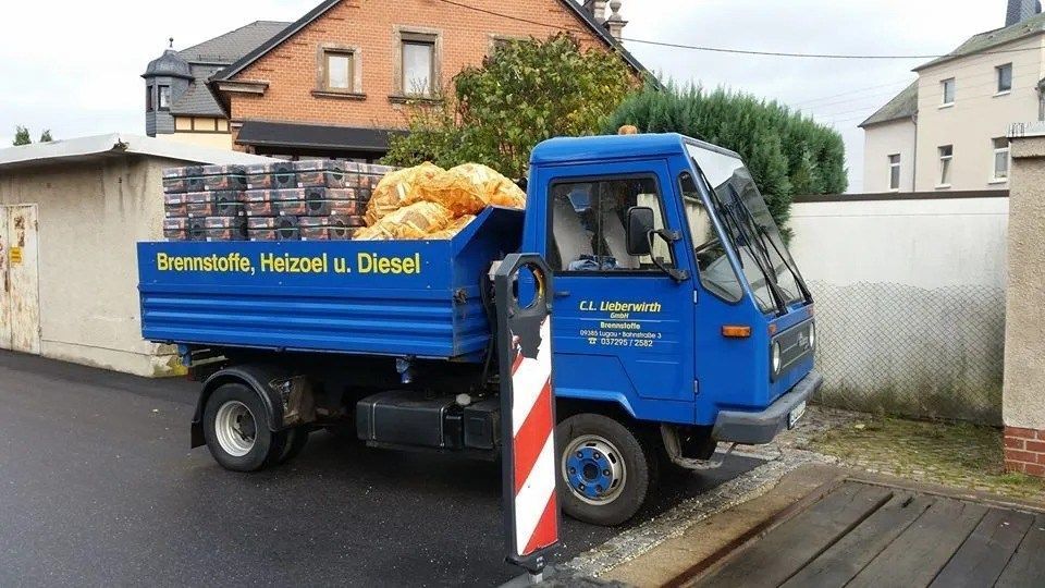 Ein blauer Muldenkipper, beladen mit Steinen, steht in einer Wohnstraße neben Häusern und einem Bordstein.