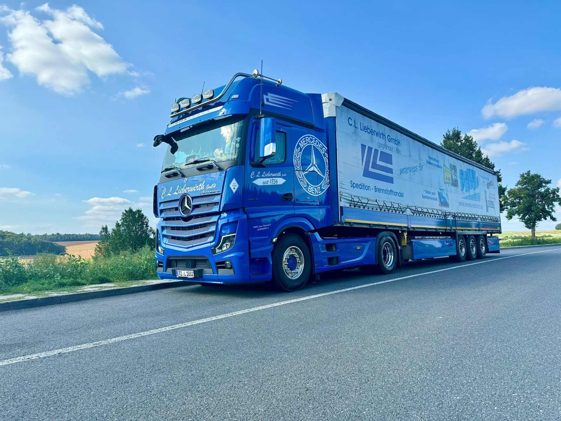 Ein blauer Sattelzug fährt auf einer Landstraße unter strahlend blauem Himmel