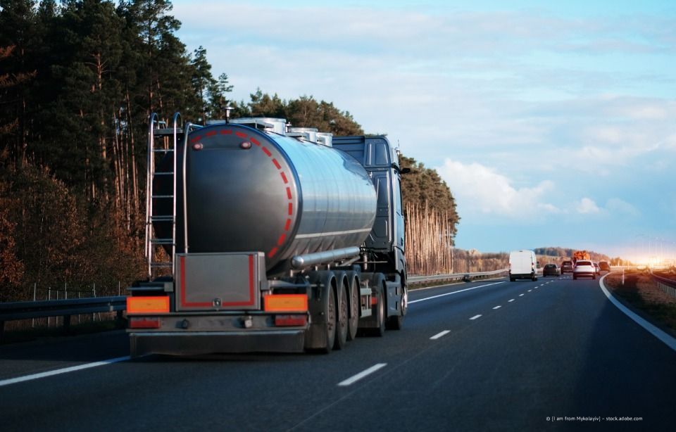 Ein silberner Tankwagen fährt bei Sonnenuntergang auf einer Autobahn neben Bäumen.