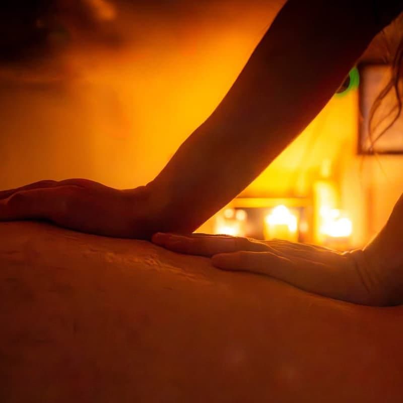 Persona recibiendo un masaje de hombros con los ojos cerrados; manos del masajista en la espalda.