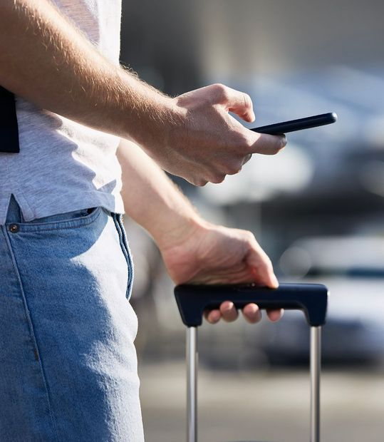 Une main qui tient un téléphone et l'autre la poignée d'une valise à roulette