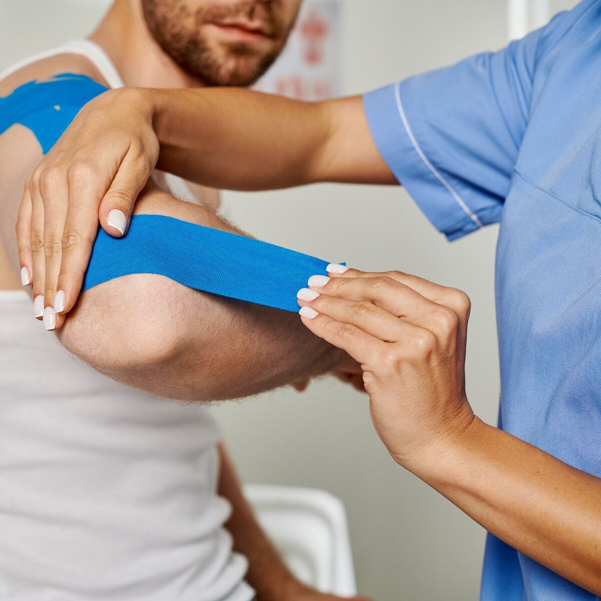 Una enfermera está colocando cinta kinesiológica azul en el brazo de un hombre.