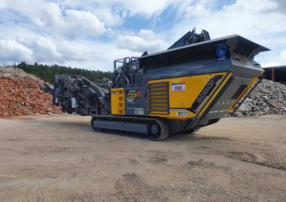 Gelb-schwarzer mobiler Steinbrecher auf Raupenketten, der Schutt verarbeitet.