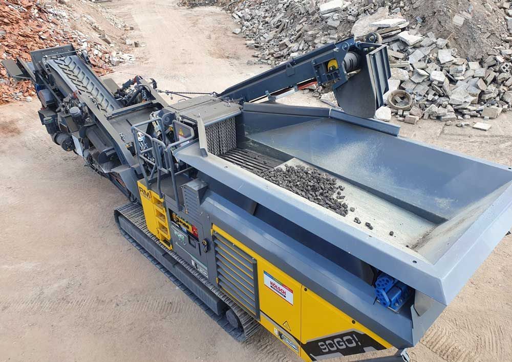 Mobiler Steinbrecher zum Sortieren von Schutt auf einer Baustelle; grau-gelbe Maschine.