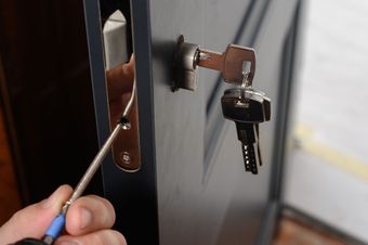 Une personne installant une serrure dans une porte, avec un tournevis.