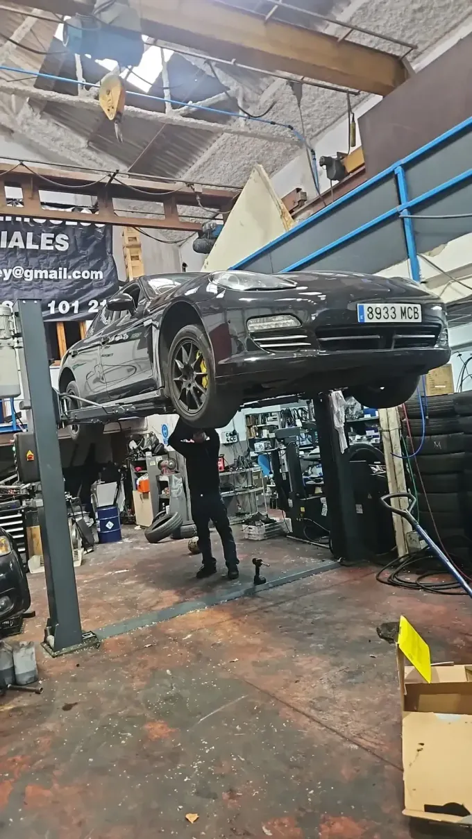 Coche en un elevador en un taller de reparación; mecánico trabajando debajo de él.