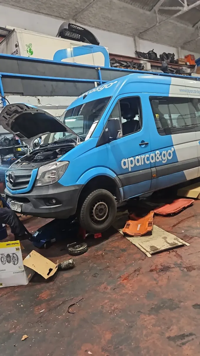 Una furgoneta azul y blanca en un taller con el capó abierto. Una persona está trabajando en el motor.