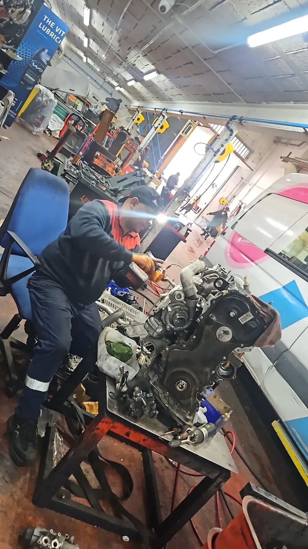 Un mecánico trabaja en el motor de un coche en un garaje desordenado, vistiendo un uniforme.