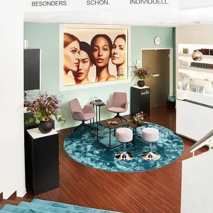 Ein moderner Empfangs- oder Wartebereich mit einem großen Porträtfoto an der Wand und stilvollen rosa Sesseln.