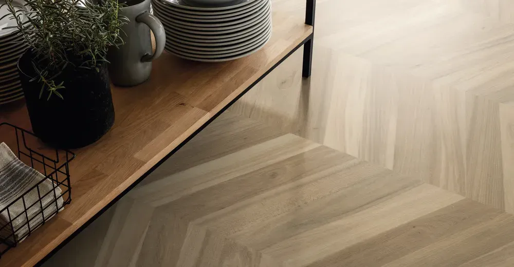Nahaufnahme eines hochwertigen Holzbodens (Parkett oder Vinyl) im Fischgrät-Muster, kombiniert mit einer hellen Wand.