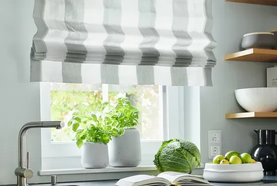 Ein quergestreiftes Faltrollo in Grau und Weiß, montiert über einem Küchenfenster mit frischen Kräutern.