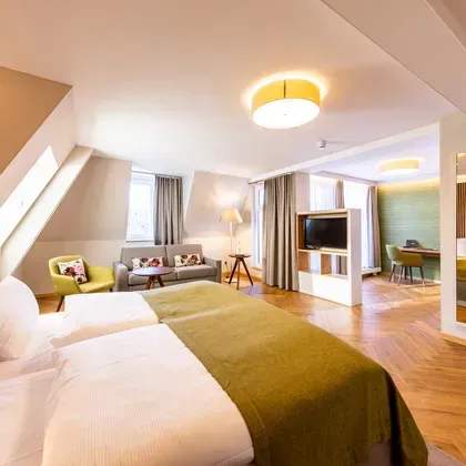 Ein helles Hotelzimmer mit Dachschräge, gemütlichem Sofa und warmem Beleuchtungskonzept für eine wohnliche Atmosphäre.