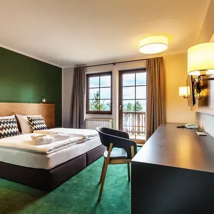 Ein Schlafzimmer mit dunkler Akzentwand, Holzelementen am Fenster und klassischen, warmen Leuchten.