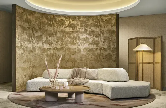 Eine gebogene Wand mit einer golden schimmernden Strukturtapete in einem luxuriösen Wohnbereich mit hellem Polstersofa.