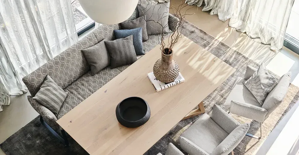 Blick von oben auf einen hellen Esstisch aus Holz mit grauen Polsterstühlen und dekorativen Vasen.