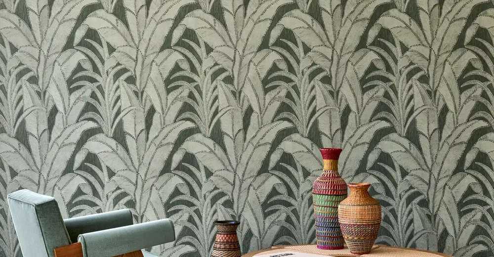 Eine Wand mit auffälligem Palmenblatt-Muster in Grüntönen, davor stehen dekorative, farbenfrohe Vasen.