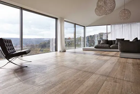 Ein minimalistisches Zimmer mit hochwertigem Holzboden und einer Panorama-Glasfront, die den Blick in die Natur freigibt.