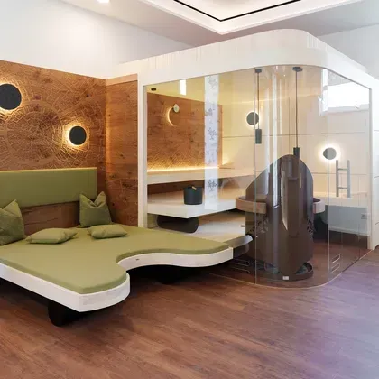 Ein moderner Wellnessbereich mit einer verglasten Sauna, indirekter Beleuchtung an den Wänden und hochwertigen Holzelementen.