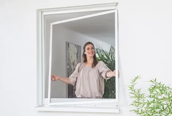 Eine Frau öffnet ein Fenster, in dem ein fester Insektenschutz-Spannrahmen montiert ist.