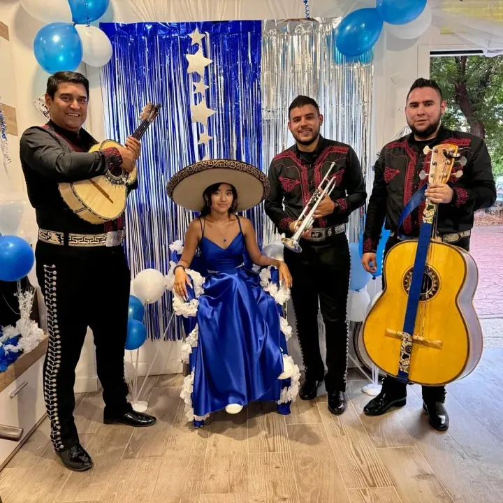 Una mujer con un vestido azul está sentada en una silla rodeada de músicos que tocan instrumentos.